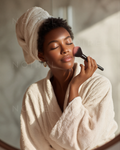 Beige towel wrap; makeup brush applying foundation near cheek