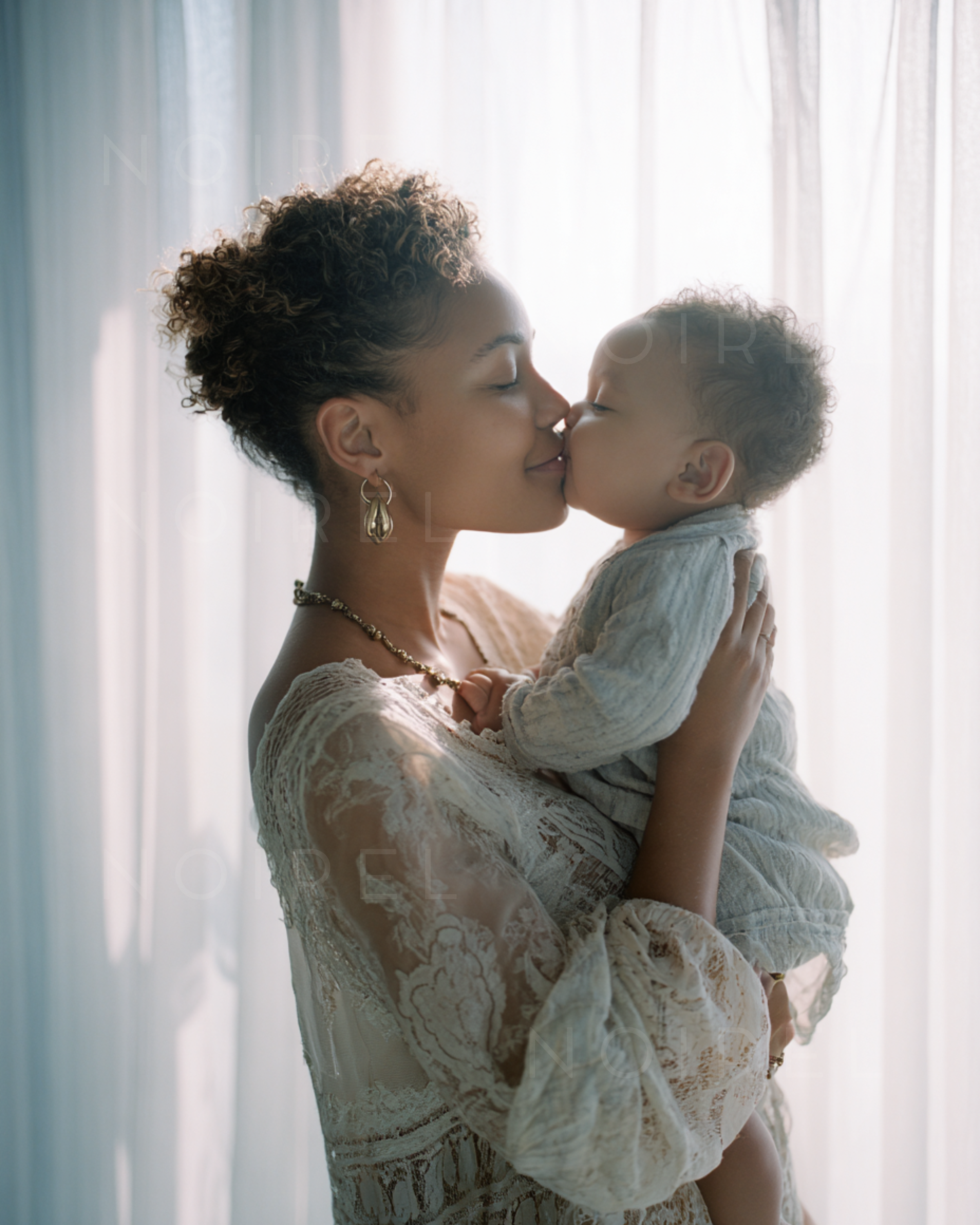 Light lace dress and matching shawl; woman holding a child close in a kiss