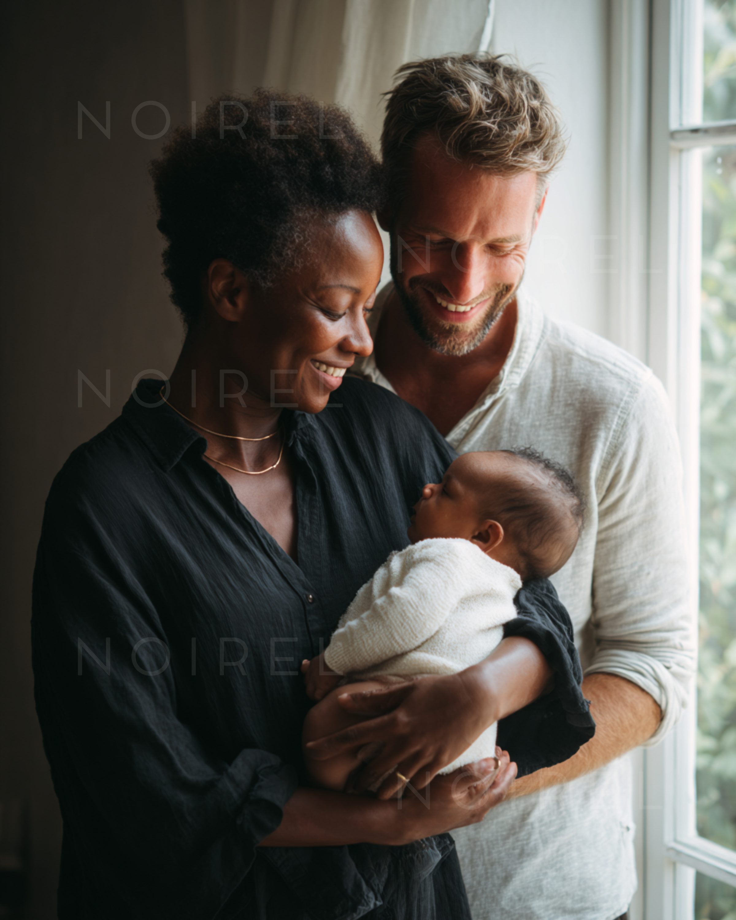 Family holding a newborn baby in a cozy embrace near a window